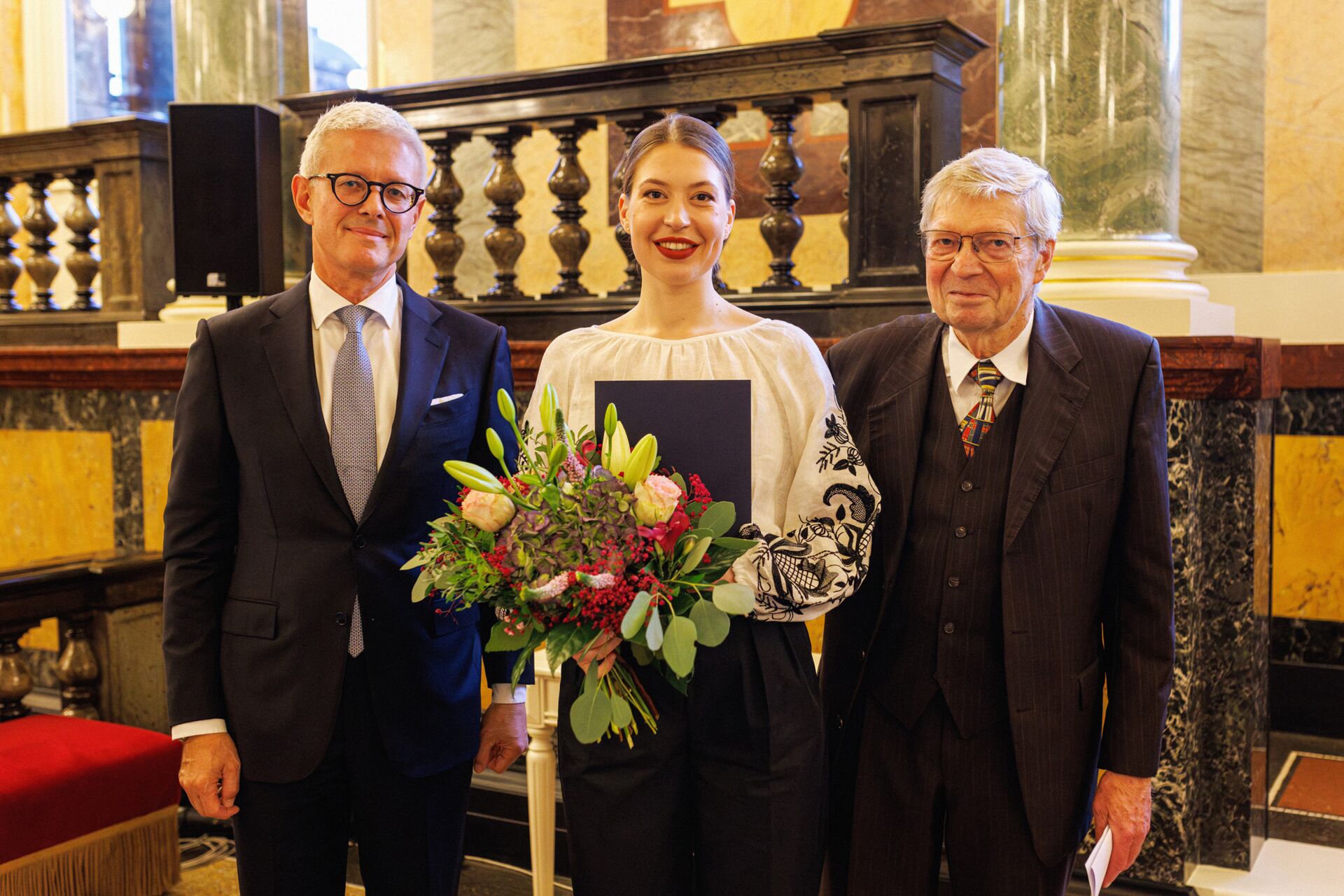 Mezzosopranistin Nicole Chirka steht mit einem Blumenstrauß zwischen Dr. Christian Zwade, Kuratoriumsvorsitzender, und Hartwig Sprau