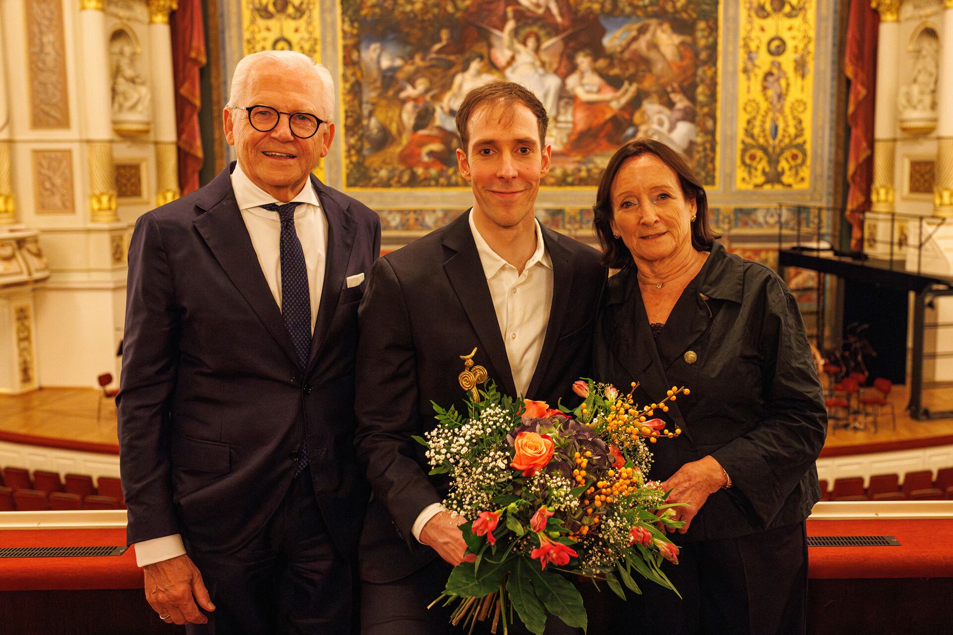 Christian Bauch mit einem Blumenstrauß zwischen Prof. Dr. Rüdiger Grube, Vorsitzender des Stiftungsrats, und Susanne Häussler